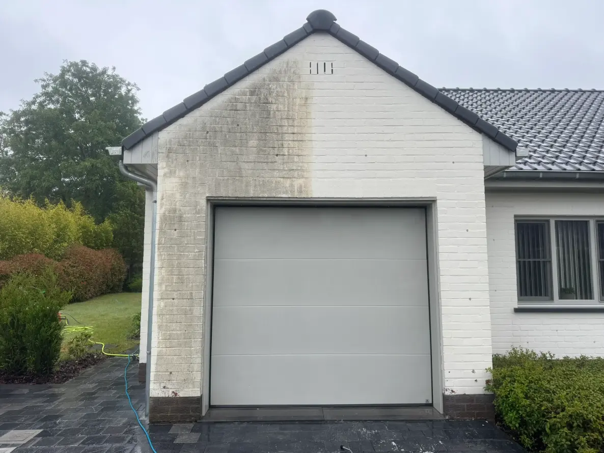 Half gereinigde witte gevel tijdens testreiniging, duidelijk verschil zichtbaar tussen vervuilde en schone zijde