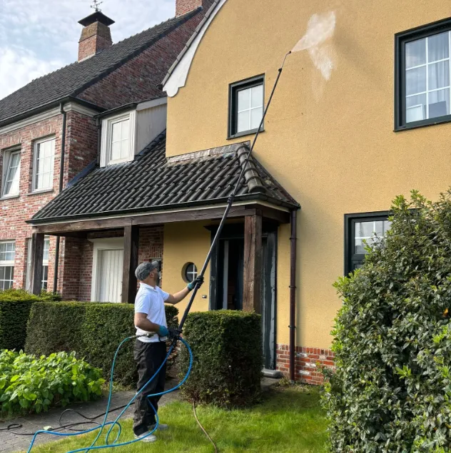 Specialist van mos reinigingsservice reinigt een gele crepi gevel met een telescopische lans