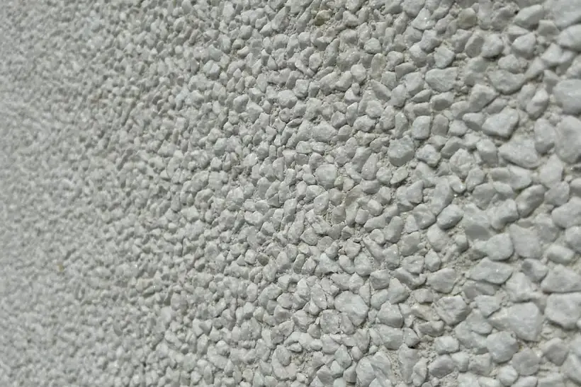 Close-up van de open korrelstructuur van witte crepi in strijklicht.