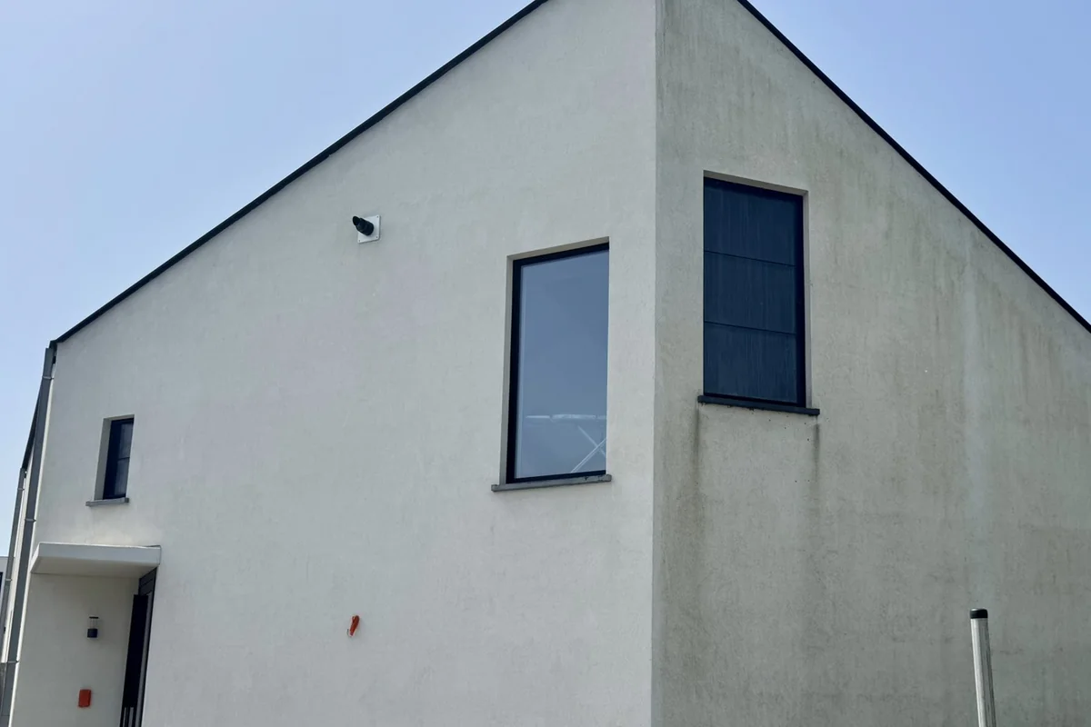 Moderne crepiwoning met een puntgevel: de rechterzijgevel is grauw, het vlak ernaast is nog wit.
