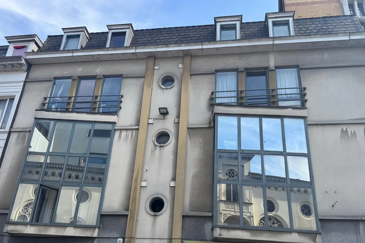 Gepleisterde stadsgevel met vlekkerige, verweerde afwerking en donkere regensporen onder de raamdorpels.