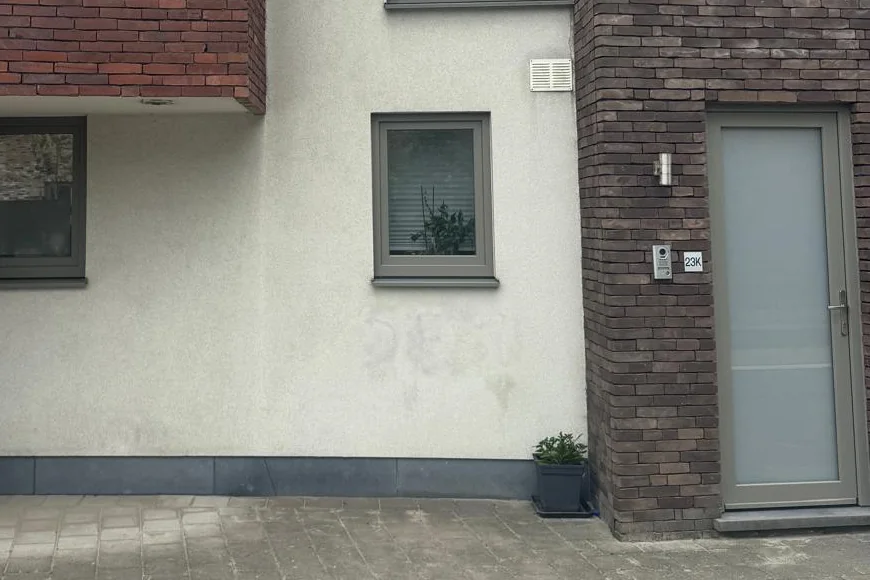 Lichtgrijze crepigevel tussen twee bakstenen gevels; onder het raam tekent zich nog vaag af waar graffiti heeft gestaan.