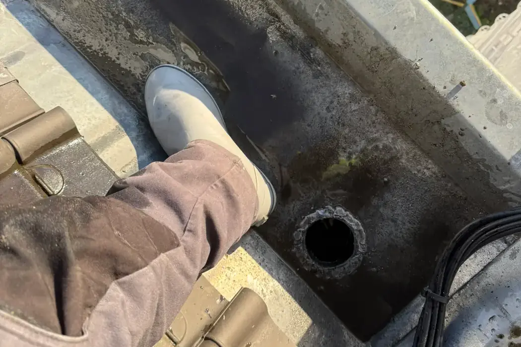 Blik in een gereinigde dakgoot met een vrije afvoeropening, gezien vanaf de dakrand.