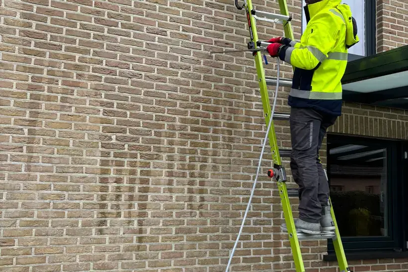 Medewerker van MOS Reinigingsservice die vanaf een ladder een bakstenen gevel behandelt.