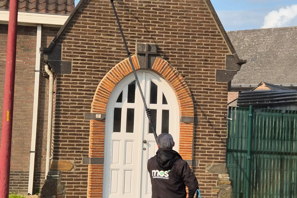 Medewerker van MOS Reinigingsservice die met een telescopische lans vanaf de grond de bakstenen puntgevel van een woning reinigt.