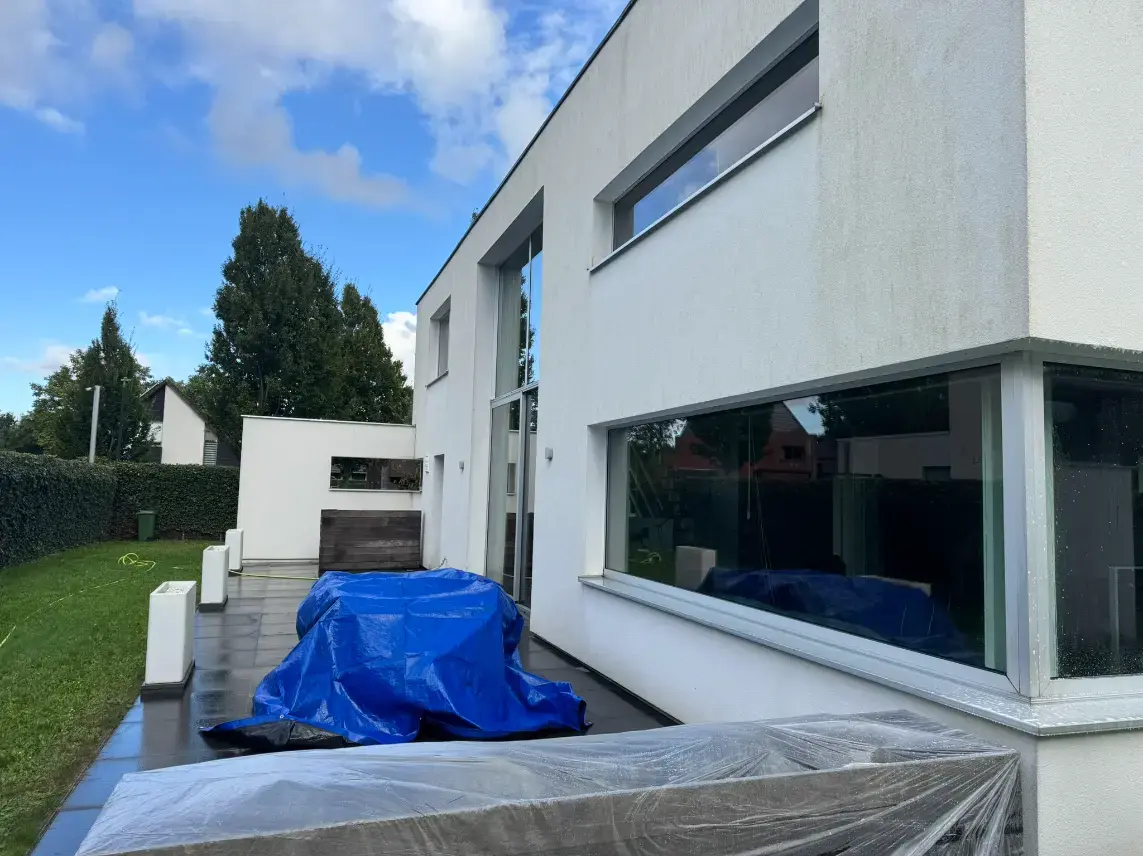 Tuinmeubelen naast een crepigevel afgedekt met folie en een dekzeil.