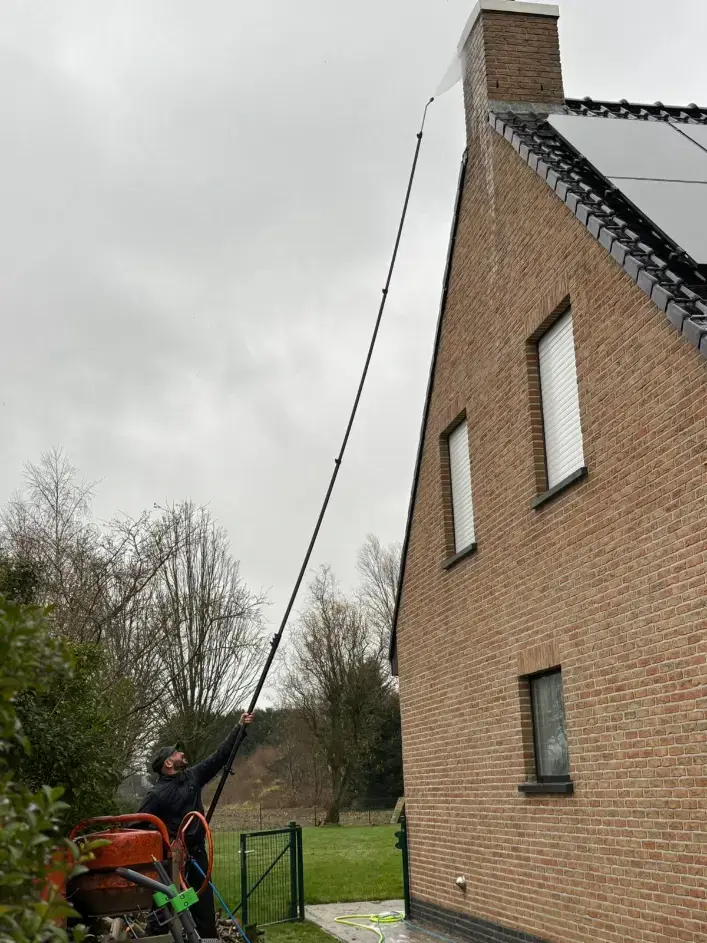 Een medewerker bedient een telescooplans vanaf de grond bij een bakstenen gevel.