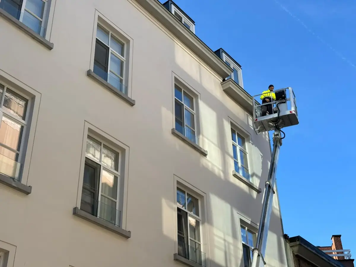 Medewerker in de bak van een hoogtewerker aan een hoge gevel in Gent.
