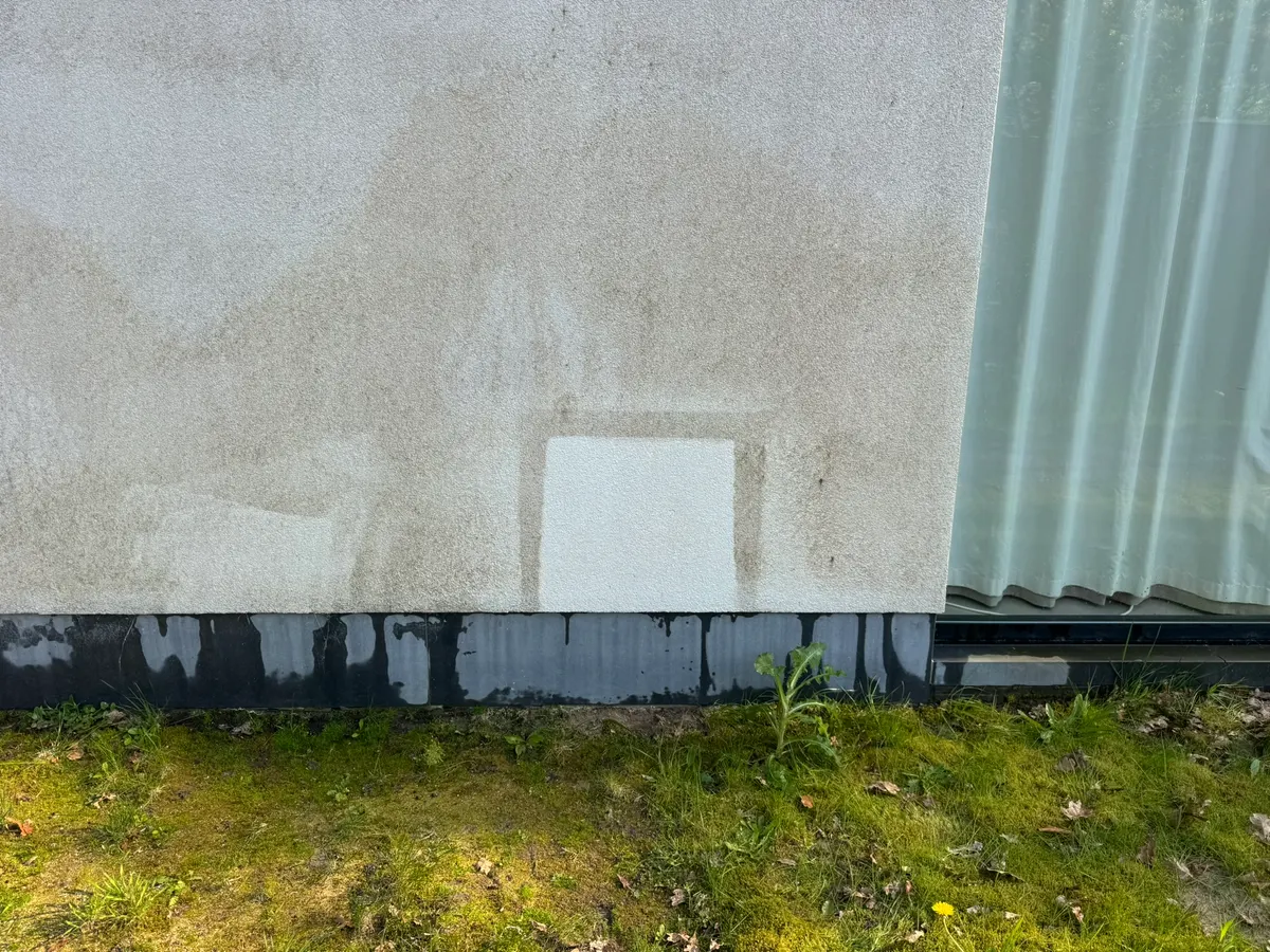 Grauwe crepigevel met onderaan een klein gereinigd vierkant, waar de lichte kleur weer zichtbaar is.
