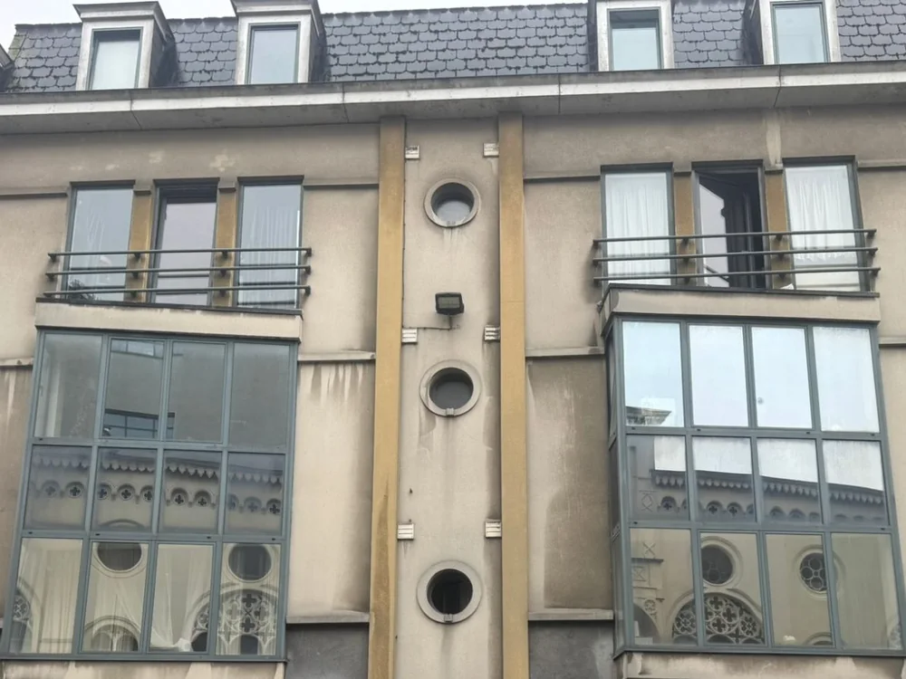 Stadsgevel in Gent vóór het werk: grauw pleisterwerk met donkere regensporen onder de ramen.