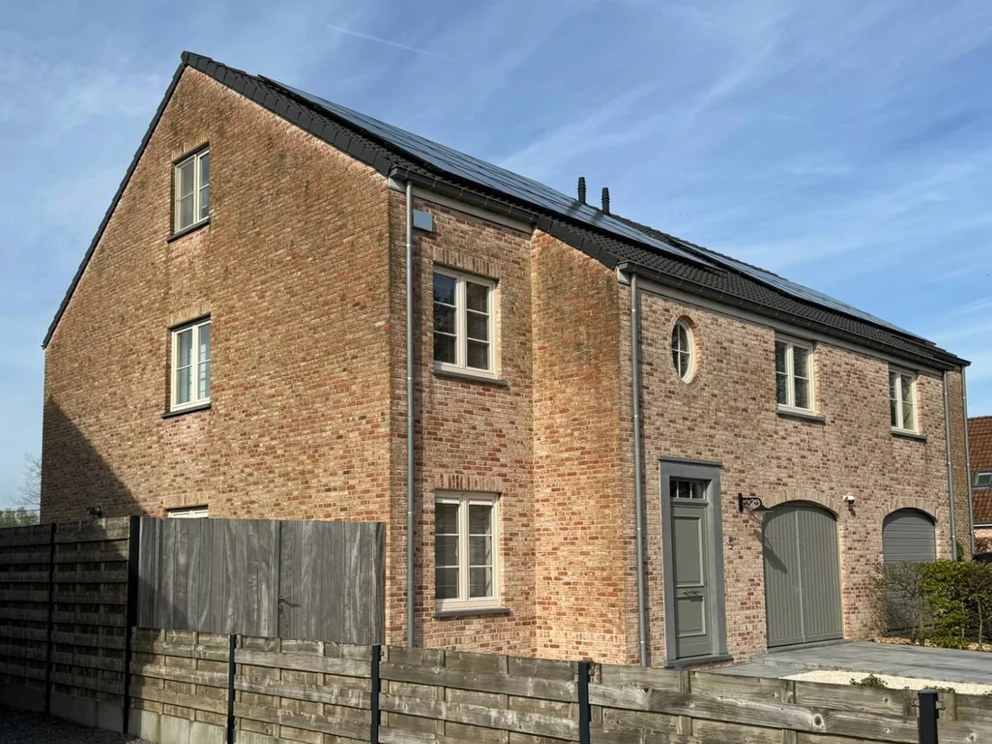 Bakstenen woning met een hoge topgevel en zonnepanelen op het dak, in de zon.