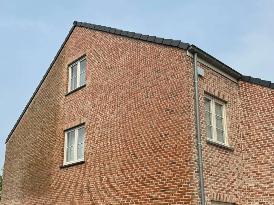 Topgevel in rode baksteen met een donkere, groenige zone aan de linkerkant.