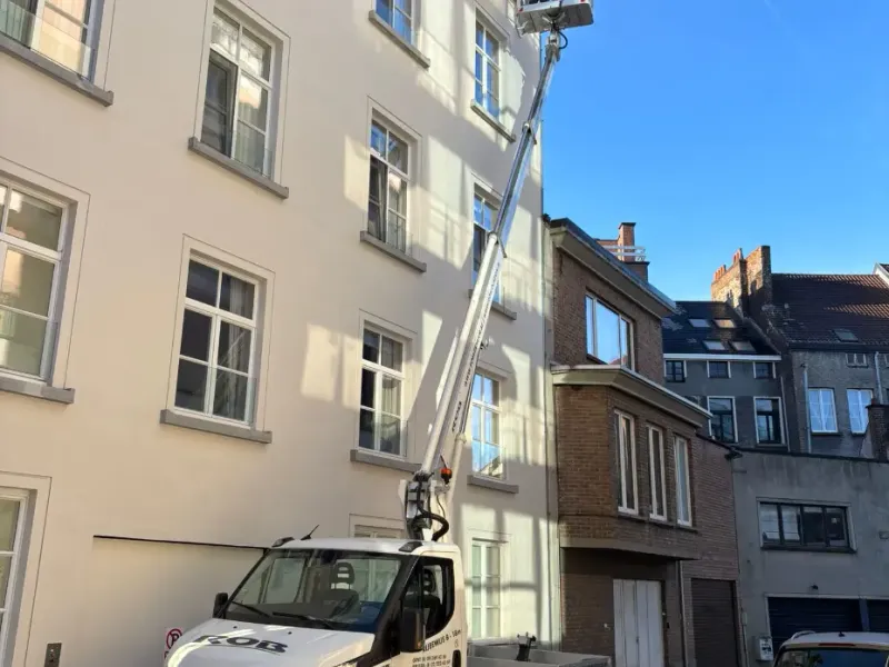 Hoogtewerker uitgeschoven langs een hoge gevel in Gent om de dakgoot te bereiken.
