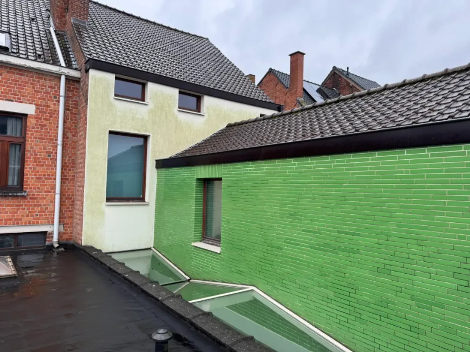 Crèmegrauwe crepigevel met groene aanslag naast een groene aanbouw in Gentbrugge.