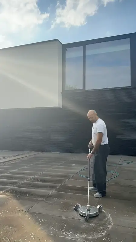 Een terrasreiniger op natte betontegels van een terras.