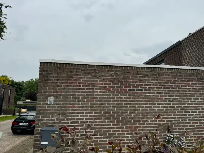 Zijgevel bakstenen woning met vervuiling vóór reiniging